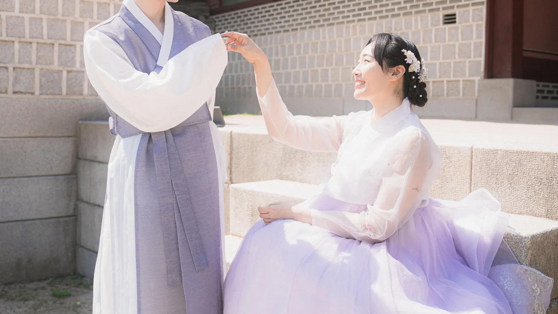A couple in pale hanbok posing on the steps of a palace building, from the hanbok photoshoot listing