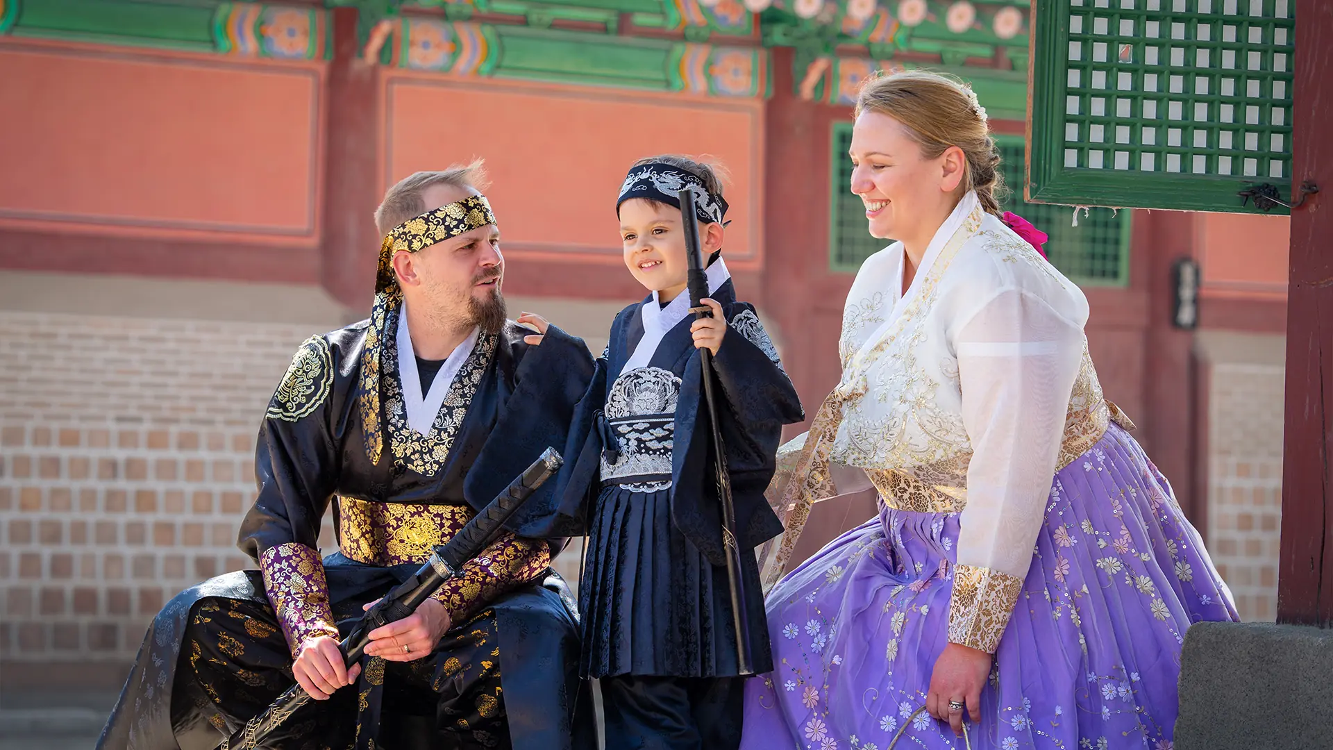 A family in rented hanbok, a king's robe, a child's outfit and a lilac skirt, in front of a palace hall, from the hanbok rental listing